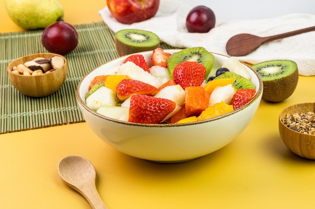 Salada de frutas frescas em uma tigela Frutas tropicais e multicoloridas Abacaxi manga uva morango mamão melão kiwi Adicional com castanhas e granola Foco seletivo