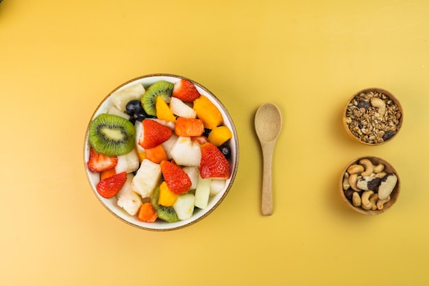 Salada de frutas frescas em uma tigela Frutas tropicais e multicoloridas Abacaxi manga uva morango mamão melão kiwi Adicional com castanhas e granola Vista superior Foco seletivo