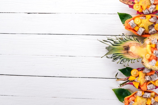 Salada de frutas tropicais servida em metade de uma fruta do dragão mamão rambutan tamarindo cacto manga de frutas em um fundo de madeira vista superior