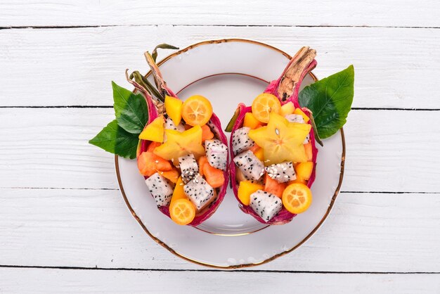 Salada de frutas tropicais servida em metade de uma fruta do dragão mamão rambutan tamarindo cacto manga de frutas em um fundo de madeira vista superior