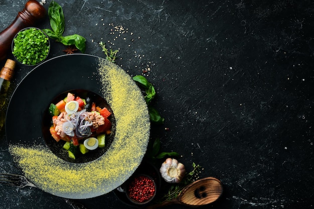 Salada de legumes com atum em um prato preto Vista superior Estilo rústico