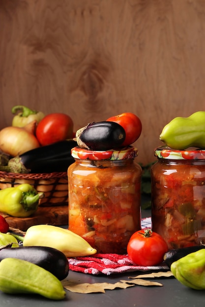 Salada de legumes com berinjela, pimentão, cebola e tomate em potes de vidro sobre mesa de madeira, formato vertical