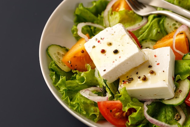 Salada de legumes com cubos de queijo feta em tigela branca sobre fundo azul Fechar