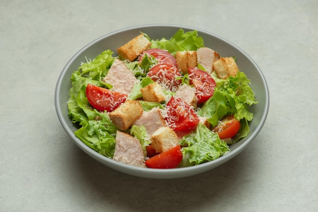 Salada de legumes com frango e queijo em uma mesa cinza Salada Caesar em um prato cinza