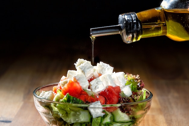 Salada de legumes com queijo temperado com azeite de oliva. Mesa de madeira escura