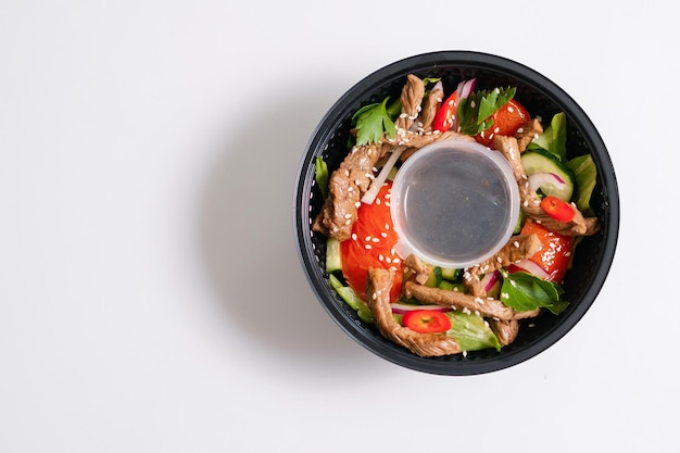 Salada de legumes com tomate e carne e gergelim em uma tigela descartável closeup