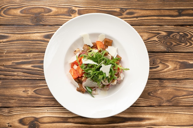 Salada de legumes com tomate, rúcula, frango, queijo parmesão e croutons de centeio em um prato de cerâmica branca