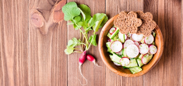 Salada de legumes da Quaresma primavera de pepino, rabanete, verduras e pão de centeio em uma placa de madeira.