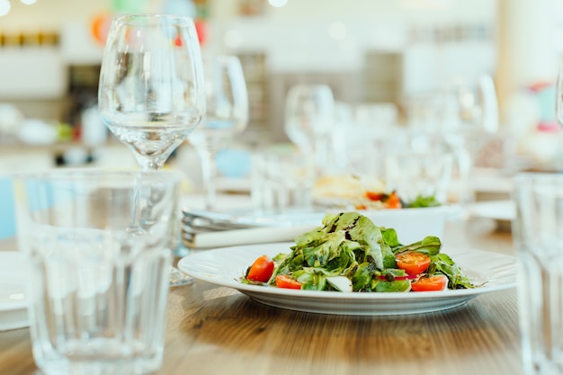 Salada de legumes e verde fresca com pesto entre copos de vinho e água - um prato em um restaurante vegetariano