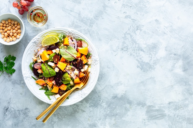 Salada de legumes fresca com beterraba, rúcula, cebola roxa, azeda, grão de bico, pêssegos e uvas em um prato branco sobre uma superfície de pedra branca. Vista do topo