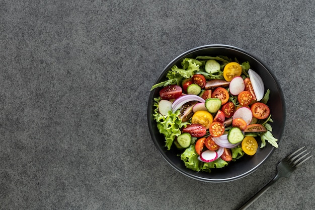 Salada de legumes fresca em um prato sobre uma superfície preta. Vista do topo