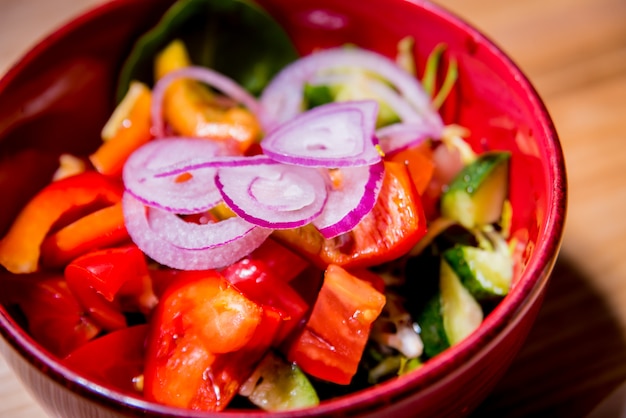 Salada de legumes fresca no prato vermelho em cima da mesa de madeira. Restaurante.