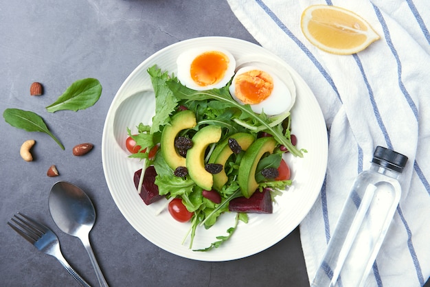 Salada de legumes fresca saudável com ovo, tomate, abacate, espinafre, alface no prato na mesa.