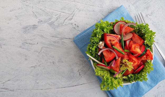 Salada de legumes frescos em um copo branco em um guardanapo azul. Vista de cima.