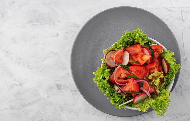 Salada de legumes frescos em um copo branco sobre um prato cinza. Vista de cima.