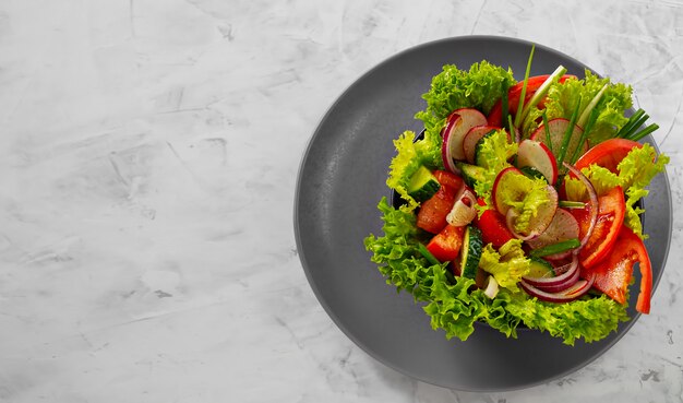 Salada de legumes frescos em um copo branco sobre um prato cinza. Vista de cima.