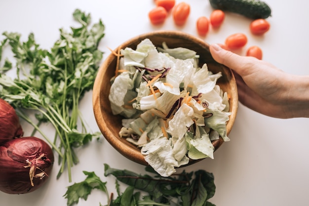 Salada de legumes saudável em uma tigela de madeira com ingredientes em uma mesa branca