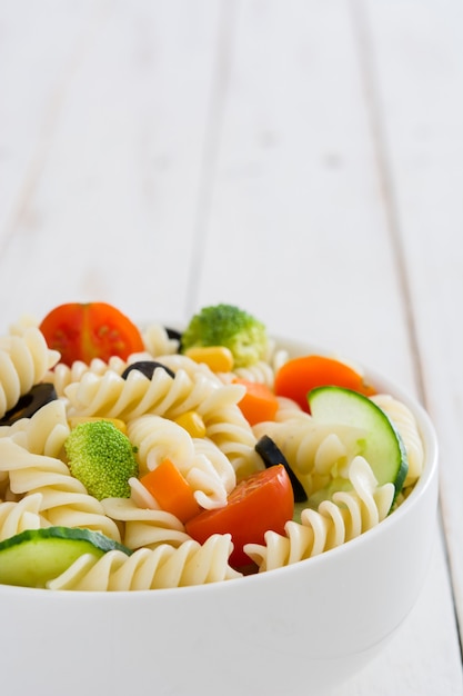 Salada de macarrão em uma tigela sobre uma mesa de madeira branca