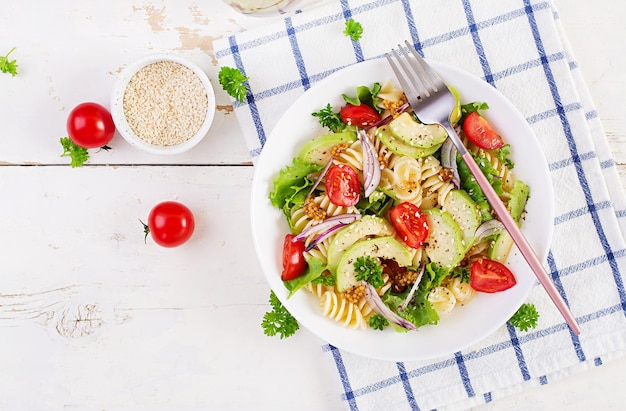 Salada de macarrão Fusilli com tomate abacate alface verde fresca, cebola vermelha e molho de mostarda em fundo branco Almoço saudável vegetariano Vista superior plana lay