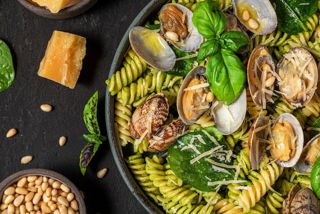 Salada de macarrão fusilli, vongole de frutos do mar, espinafre, queijo parmesão e pinhão em um prato na mesa preta