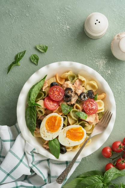 Salada de macarrão italiano Massa Orecchiette com atum, tomate, cereja, azeitona, manjericão e queijo parmesão em prato sobre pedra verde ou fundo de concreto Cozinha tradicional italiana Flat lay Espaço para cópia