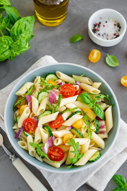 Salada de macarrão vegan saudável com tomates, pepinos, cebolas vermelhas e rúcula em uma tigela copie o espaço