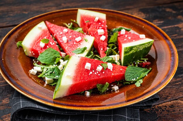 Salada de melancia fresca no verão com queijo feta, rúcula, cebola em um prato rústico. Fundo escuro. Vista do topo.