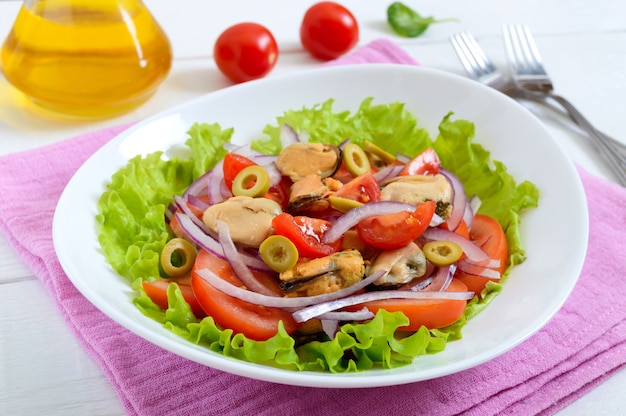 Salada de mexilhões marinados, tomate fresco, cebola roxa, azeitonas em uma tigela sobre uma mesa de madeira branca