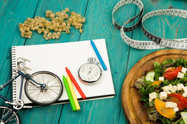 Salada de modelo de bicicleta de legumes frescos cronômetro de bloco de notas vermelho e fita métrica em uma mesa de madeira azul