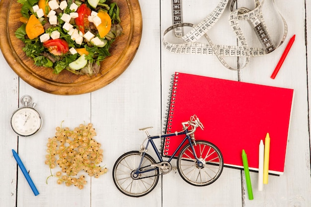 Salada de modelo de bicicleta de legumes frescos, cronômetro e fita métrica de bloco de notas vermelho