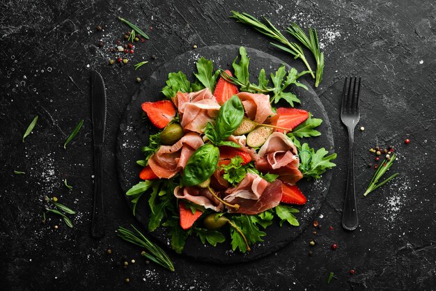 Salada de morangos e alcaparras de presunto de rúcula em uma placa de pedra preta cozinha italiana