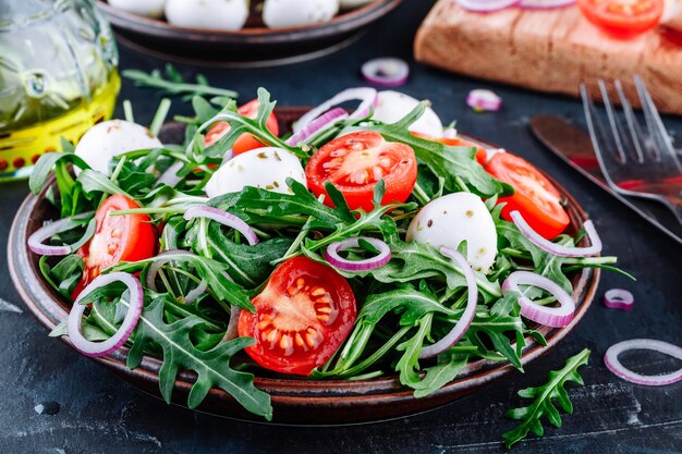 Salada de mussarela de rúcula com tomate e cebola roxa em fundo escuro