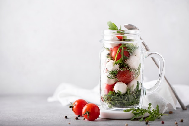 Salada de mussarela, tomate cereja e rúcula em uma caneca de vidro, sobre um fundo claro