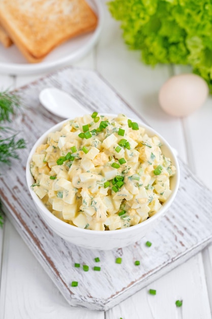 Salada de ovo com cebolinha picada por cima em uma tigela branca para cozinhar um sanduíche Foco seletivo