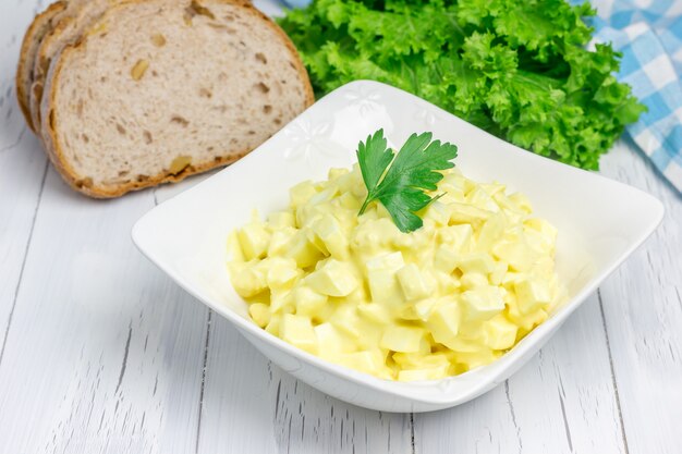 Salada de ovo em uma tigela com pão e alface no fundo