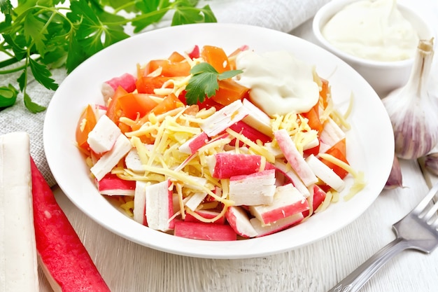 Salada de palitos de caranguejo, queijo, alho e tomate com maionese, guardanapo e salsa no fundo de uma leve placa de madeira