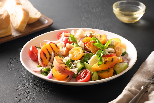 Salada de panzanella com tomate, pão, queijo e pêssego em tigela branca sobre fundo preto. Cozinha italiana. Salada de panzanella vegetariana. Comida saudável mediterrânea. Fechar-se.