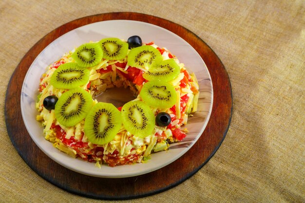 Salada de peito de frango guarnecida com kiwi e azeitonas em uma saladeira em uma toalha de mesa horizontal