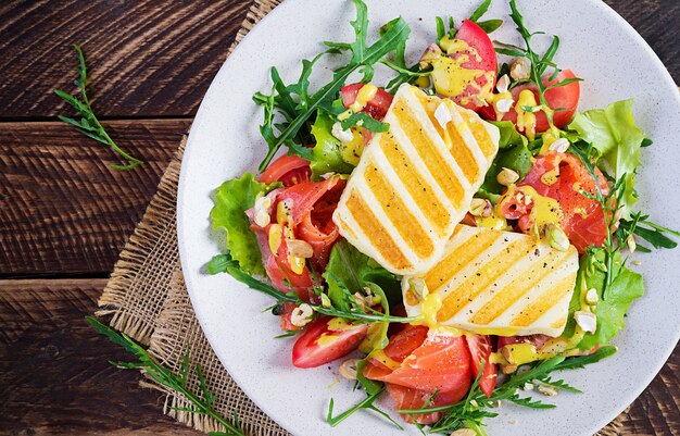 Salada de queijo halloumi grelhado com salmão salgado, tomate e ervas verdes. comida saudável no prato com fundo de madeira. vista superior, banner