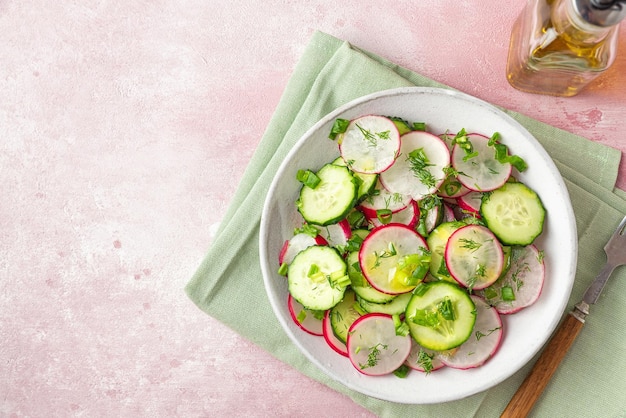 Salada de rabanete com cebola endro pepino e azeite em um prato com garfo no fundo de concreto rosa Vista superior