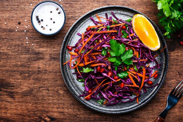 Salada de repolho com repolho roxo cenoura salsa sementes de romã e molho de azeite laranja na vista superior do fundo da mesa de cozinha de madeira