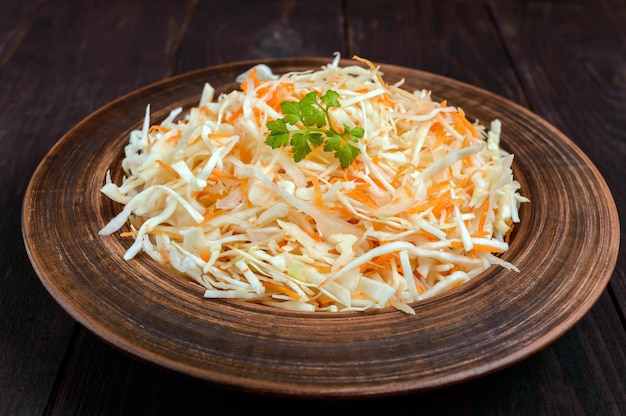 Salada de repolho fresco e cenoura em uma tigela de barro no fundo escuro de madeira Prato de vitamina vegetariana magra