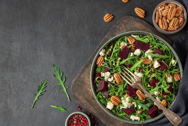 Salada de rúcula, beterraba e queijo azul com noz-pecã em um prato com garfo na mesa preta