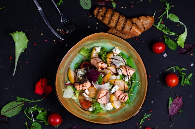 Salada de salmão fresco com pera caramelizada, queijo feta e alface em superfície escura