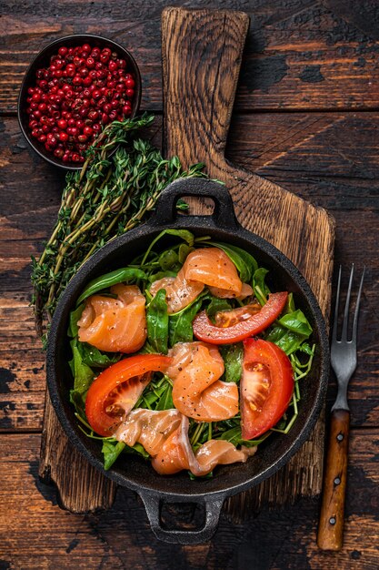 Salada de salmão fresco com rúcula, tomate e vegetais verdes. fundo de madeira escuro. vista do topo.