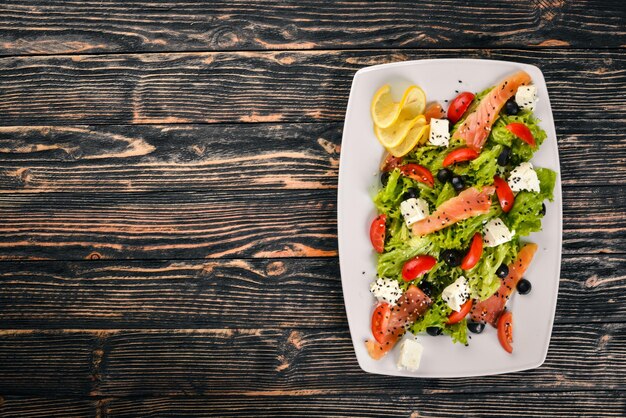 Salada de salmão salada de queijo feta folhas e legumes frescos no prato Em um fundo de madeira Vista superior Espaço livre para texto