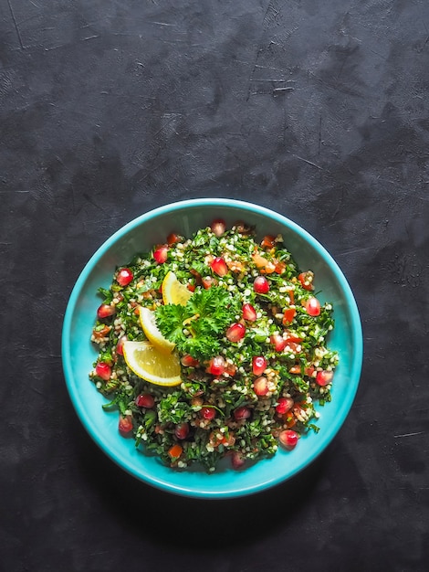 Salada de tabule com cuscuz em uma tigela em cima da mesa preta. Levantine salada vegetariana com salsa, hortelã, bulgur, tomate.