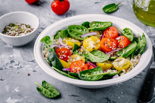 Salada de tigela verde saudável com espinafre quinoa tomate amarelo e vermelho cebolas e sementes em fundo cinza