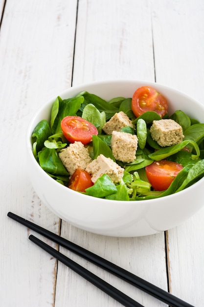 Salada de tofu vegan com tomate e alface de cordeiro na mesa de madeira branca