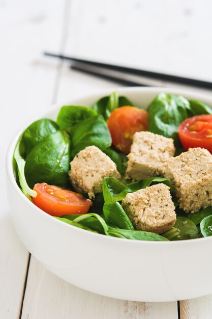 Salada de tofu vegan com tomate e alface de cordeiro na mesa de madeira branca